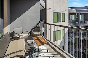 A balcony with wicker furniture, a wooden table, and a view of a multi-story building. - Escape To The Sage Room 2 BR Suite Tempe Town Lake (Tempe)