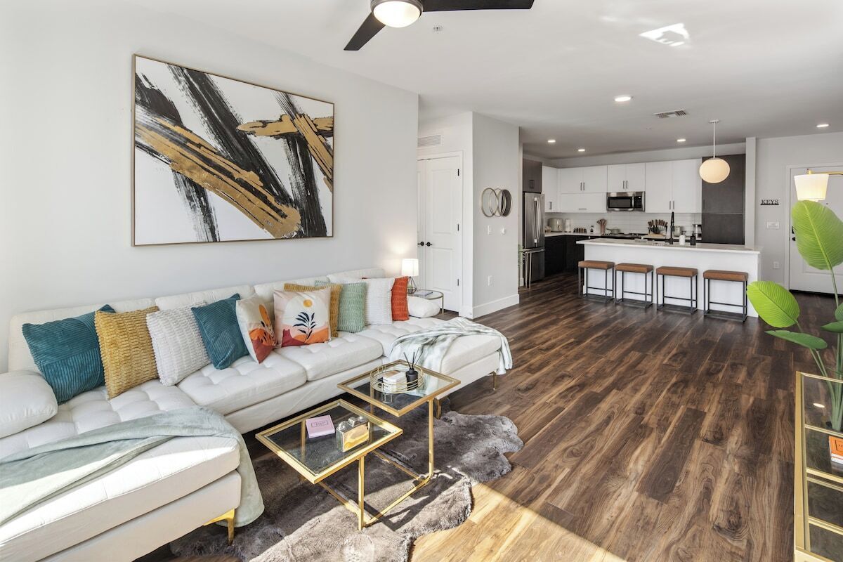 Ein modernes Wohnzimmer mit einem weißen Sofa, einem Glastisch und einem großen, abstrakten Gemälde an der Wand.