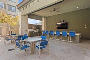 Une terrasse extérieure équipée d’un barbecue, d’un coin salon et d’un téléviseur fixé au mur.