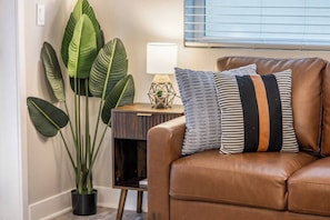 Ein braunes Ledersofa mit gestreiften Kissen, ein Blumentopf und eine Lampe auf einem Holztisch.
