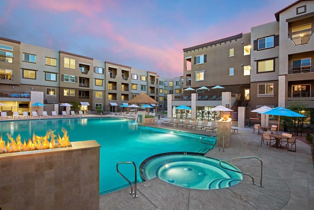 A hotel pool area with a hot tub, lounge chairs, and umbrellas.