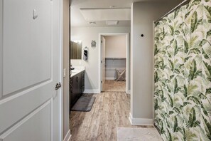A hallway leading to a kitchen with a wooden floor, a white door, and a shower curtain with a leaf pattern. - Escape To N. Scottsdale Modern & Chic 1BR Suite (Phoenix)