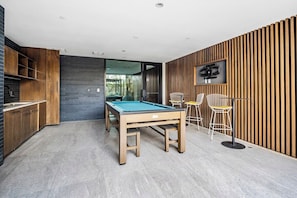 A modern kitchen with a pool table, wooden cabinets, and a TV mounted on the wall. - Escape To Poolside Bohemian Desert King Bed Studio (Tempe)