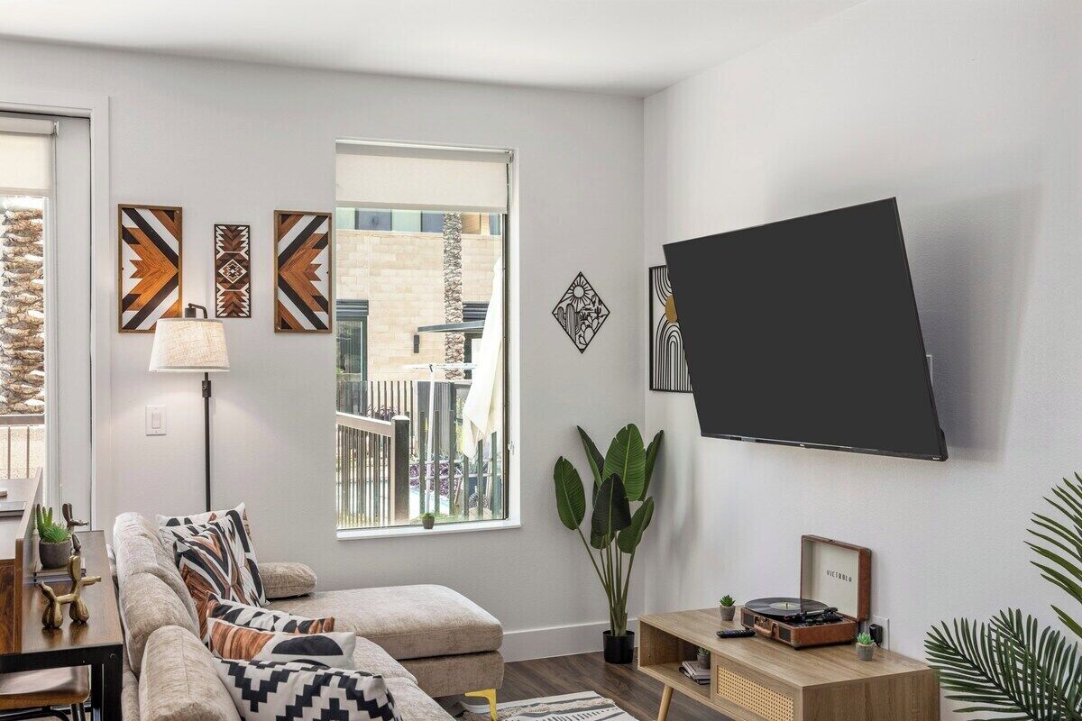 Ein Wohnzimmer mit einer Couch, einem Couchtisch, einem an der Wand montierten Fernseher und einem Fenster mit Blick auf ein Gebäude.