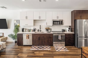 A modern kitchen with white cabinets, stainless steel appliances, and a wooden floor. - Escape To Poolside Bohemian Desert King Bed Studio (Tempe)