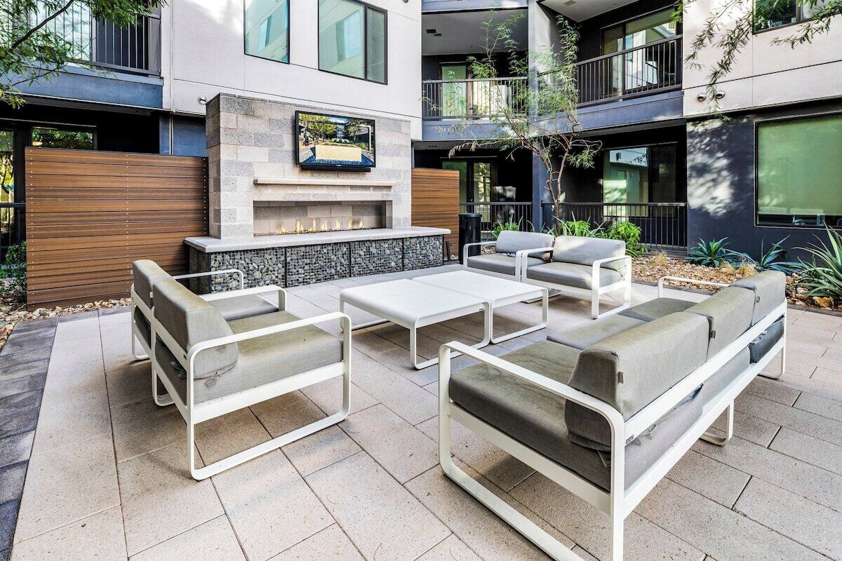 A modern outdoor seating area with a fireplace, cushioned sofas, and a flat-screen TV mounted above the fireplace.