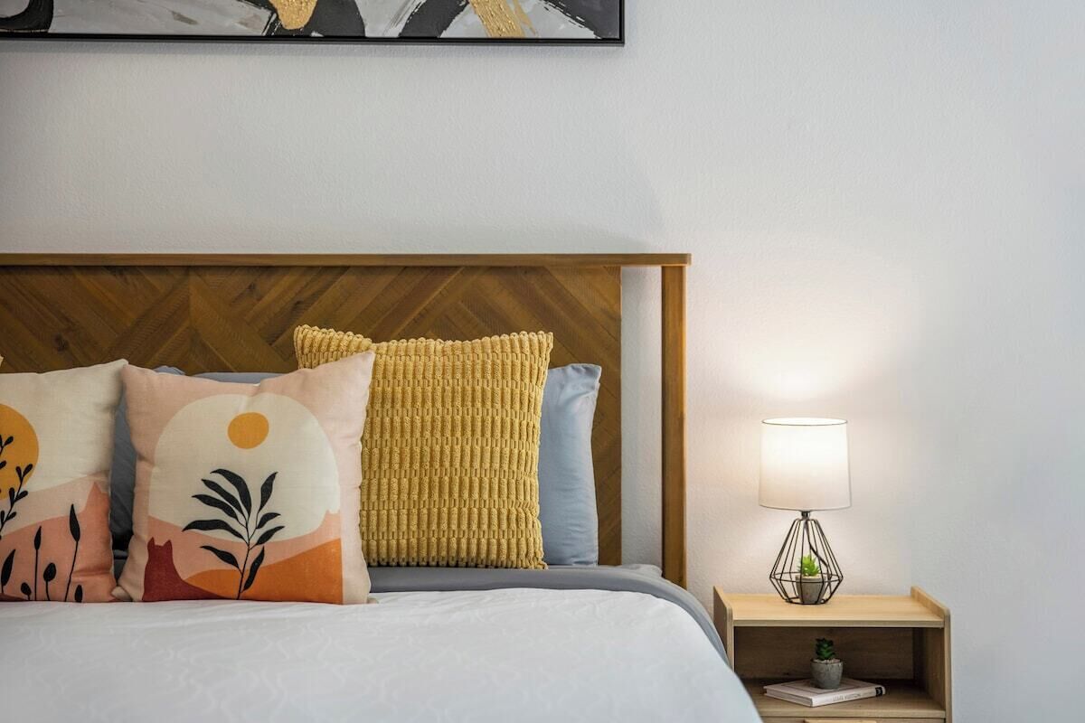 Un letto rifatto con cuscini decorati, una testiera in legno e un comodino con una lampada e una piccola pianta.