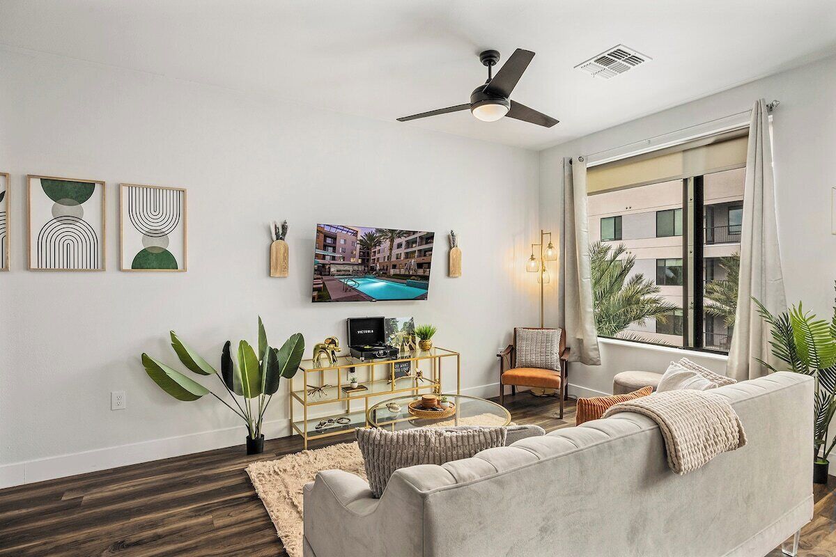 Ein modernes Wohnzimmer mit einer Couch, einem Fernseher, einem Deckenventilator und einem großen Fenster.