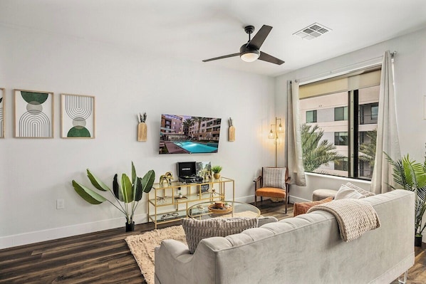 A modern living room with a sofa, a television, a ceiling fan, and a large window. - Escape To Tempe Town Lake Golden Dream Studio (Tempe)