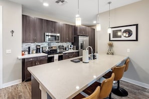 A modern kitchen with dark wood cabinets, stainless steel appliances, and a central island with bar stools. - Escape To Hollywood Hideaway 2BR King Bed Suite (Phoenix)