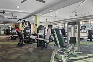 Ett gym med olika träningsmaskiner, en takfläkt och stora fönster.