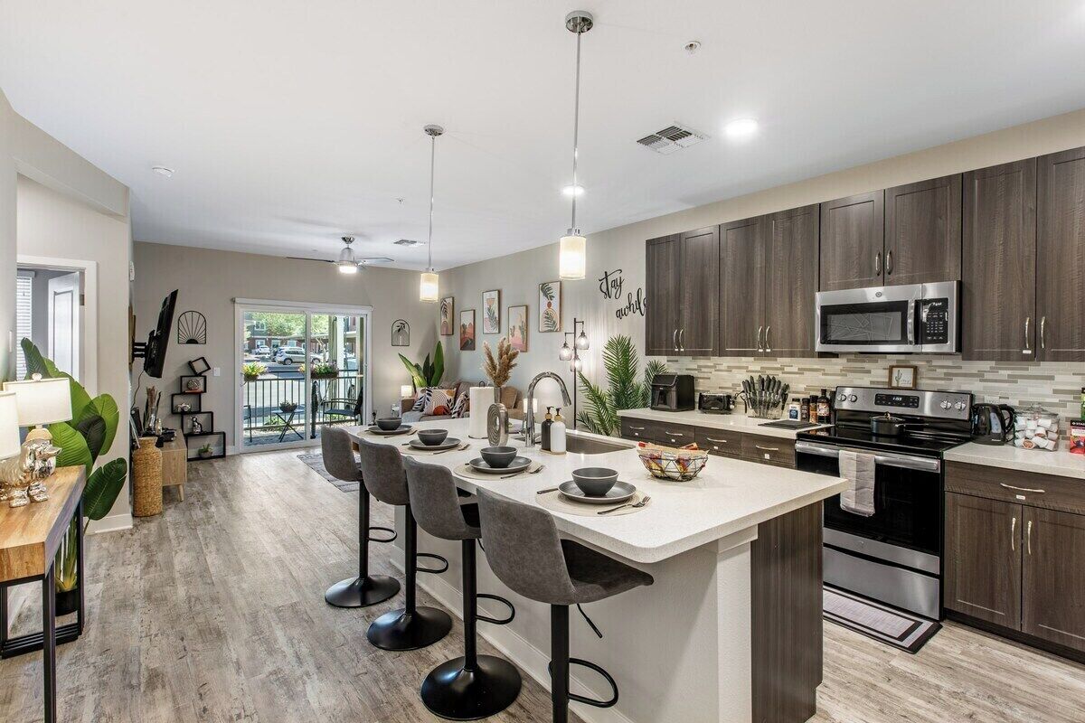 Una cocina moderna con una isla central, taburetes de bar y un área de comedor con mesa y sillas.