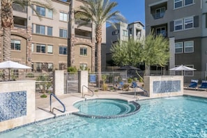A swimming pool with a circular hot tub, surrounded by a fence, with a view of multi-story buildings in the background. - Escape to N. Scottsdale 1BR Bohemian Desert Dream (Phoenix)