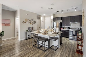 A modern kitchen with a central island, dark cabinets, stainless steel appliances, and a dining area with stools. - Escape To The Executive 2BR King Bed Uptown Suite (Phoenix)