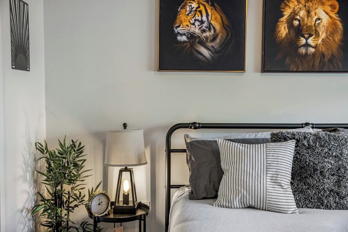 A bedroom with a bed, pillows, a nightstand with a lamp, and two framed animal portraits on the wall.