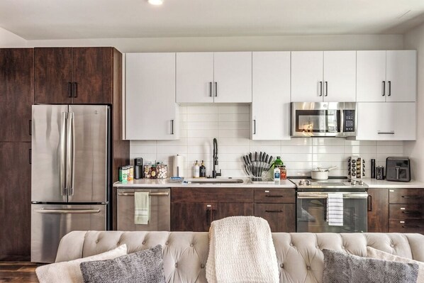 A modern kitchen with white cabinets, stainless steel appliances, and a beige sofa with throw pillows. - Escape To The Tempe Penthouse King Bed Studio (Tempe)