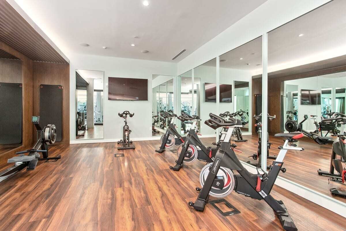 Ein Fitnessraum mit Trainingsgeräten, Holzboden und gro ßen Spiegeln.