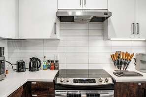 Una cocina moderna con armarios blancos, una campana extractora de acero inoxidable, un horno empotrado y una cafetera.