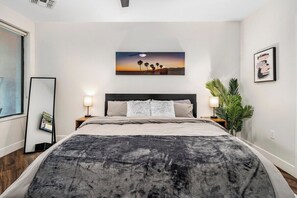Un dormitorio con una cama, una mesita de noche, una lámpara de noche, un cuadro en la pared y una ventana con persianas.