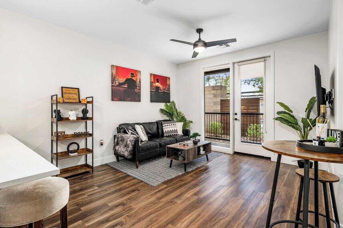 Uma sala de estar com um sofá de couro preto, uma mesa de centro, uma estante e um espaço de jantar com uma mesa redonda.