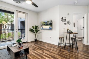 Un salón moderno con suelo de madera, una zona de comedor con taburetes, un ventanal grande y una obra de arte colgada en la pared.