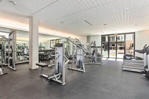 Un gimnasio moderno con diversos equipos de ejercicio, un espejo grande y vistas al exterior.