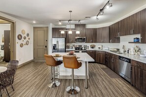 Une cuisine moderne avec des meubles en bois foncé, des appareils électroménagers en acier inoxydable et un îlot central doté de tabourets de bar.