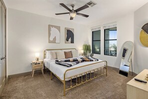 Ein Schlafzimmer mit Bett, Nachttisch, Deckenventilator, Fenster und Spiegel.