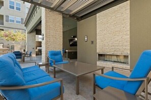 Eine Terrasse im Freien mit blauen Sitzkissen, einem Metalltisch und einer Backsteinmauer.