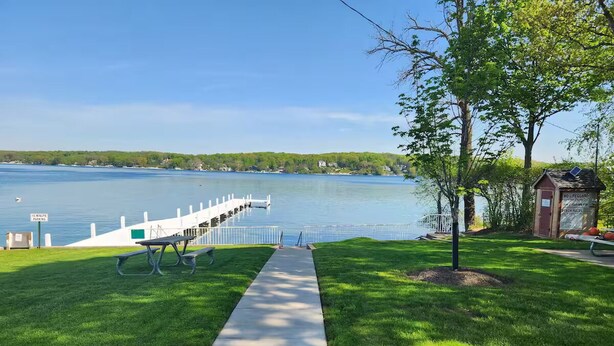 A waterfront park with a concrete pathway, picnic tables, and a lifeguard station.