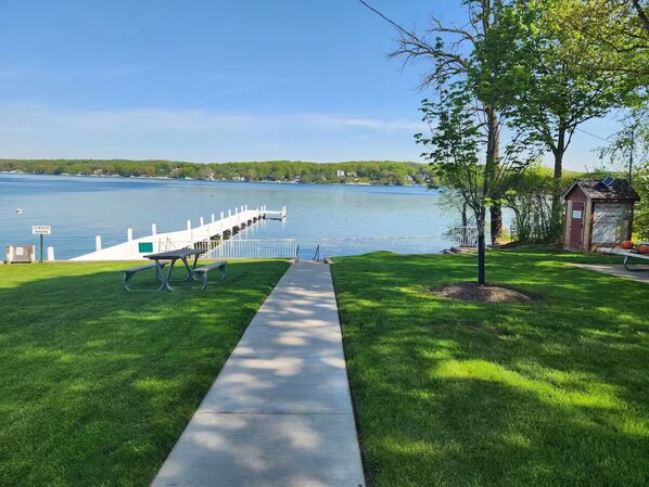 A waterfront park with a concrete pathway, picnic tables, and a lifeguard station.