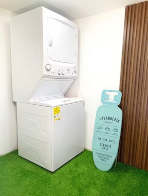 A white washing machine with a control panel, a small storage compartment, and a green grass-like floor. - Family-Friendly Apartment with Patio & Play Area in Medellín (Medellín)