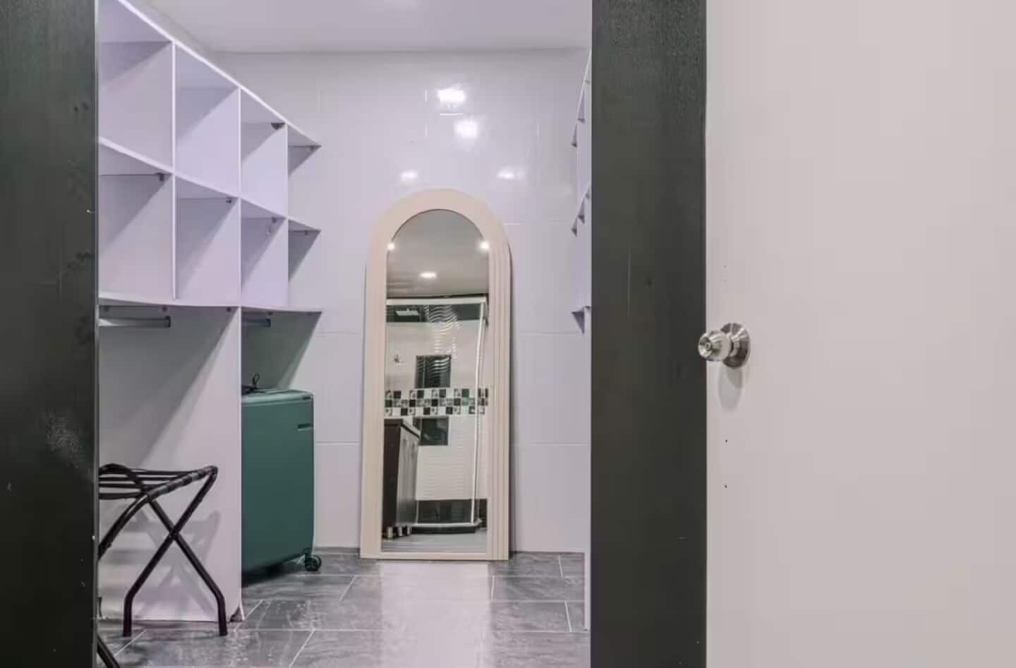 A hallway with a tiled floor, a white door with a round mirror, and a metal rack with a towel.