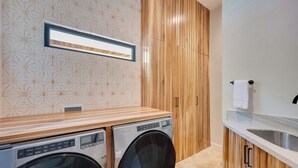 A laundry room with two front-loading washing machines, wooden cabinets, a tiled backsplash, and a countertop with a sink. - Casa VistaMar Spacious 5-bedroom villa built around a tree! (Potrero)