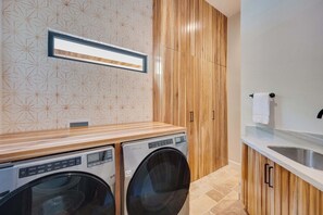 Ein Waschraum mit zwei Waschmaschinen, Holzschränken, einer gefliesten Rückwand und einer Arbeitsplatte mit Spüle.