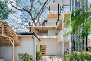 A modern multi-story building with a central staircase, a thatched-roof structure, and surrounding greenery. - Casa VistaMar Spacious 5-bedroom villa built around a tree! (Potrero)