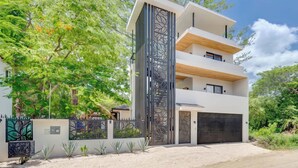 A modern multi-story residential building with a flat roof, a garage, and a decorative metal fence. - Casa VistaMar Spacious 5-bedroom villa built around a tree! (Potrero)
