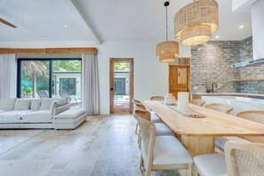 A modern kitchen with a stone backsplash, wooden cabinets, and a dining area with a long table and wicker chairs. - Casa VistaMar Spacious 5-bedroom villa built around a tree! (Potrero)