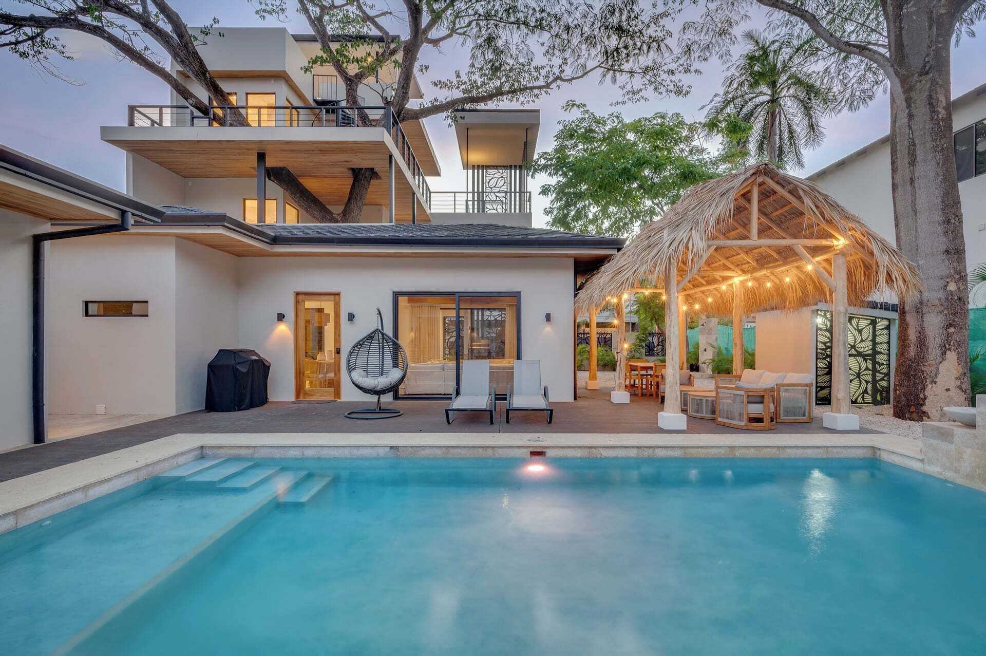 Una casa moderna con piscina, mobiliario de exterior y techo de paja.