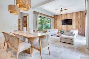 A modern living room with a sofa, a dining table with chairs, and a television mounted on a wooden wall. - Casa VistaMar Spacious 5-bedroom villa built around a tree! (Potrero)