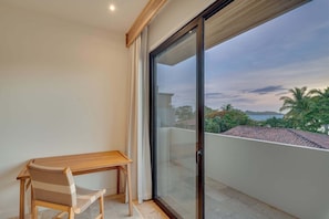 Ein Balkon mit Holztisch und Stuhl, einer Schiebeglastür und Blick auf eine Küstenlandschaft.