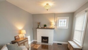 A living room with a fireplace, a sofa, a side table with lamps, and a window with blinds.