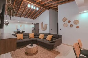 A modern living room with a sectional sofa, a round coffee table, and a dining area with a wooden table and chairs. - Stylish Boho Apartment with Mountain Views in Medellín (Medellín)