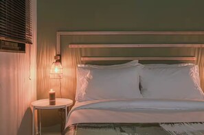 Una cama con cabecera de madera, ropa de cama blanca y una lámpara de noche.