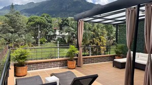 A balcony with outdoor seating, a view of a mountain, and a tennis court. - Entire Building for Groups of 16+ in Medellín (Medellín)
