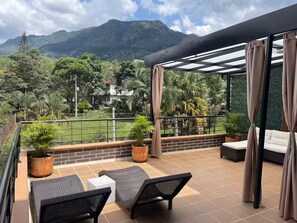 A balcony with outdoor seating, a view of a mountain, and a tennis court. - Entire Building for Groups of 16+ in Medellín (Medellín)