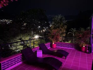 An outdoor terrace with two lounge chairs, a potted plant, and a view of a cityscape at night. - Entire Building for Groups of 16+ in Medellín (Medellín)