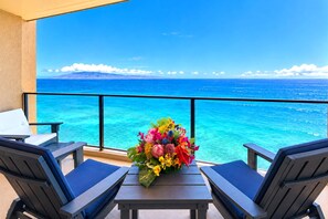 A balcony with two chairs and a table, overlooking a clear blue sea and distant mountains. - Mahana Resort | Oceanfront Studio | Car Incl. w/ 6+ Nights | MAH-1002 by KBM (Lahaina)