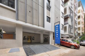 A hotel entrance with a covered outdoor area, a staircase, and a red car parked outside. - Monday Hotels & Suites Madhapur (Hyderabad)