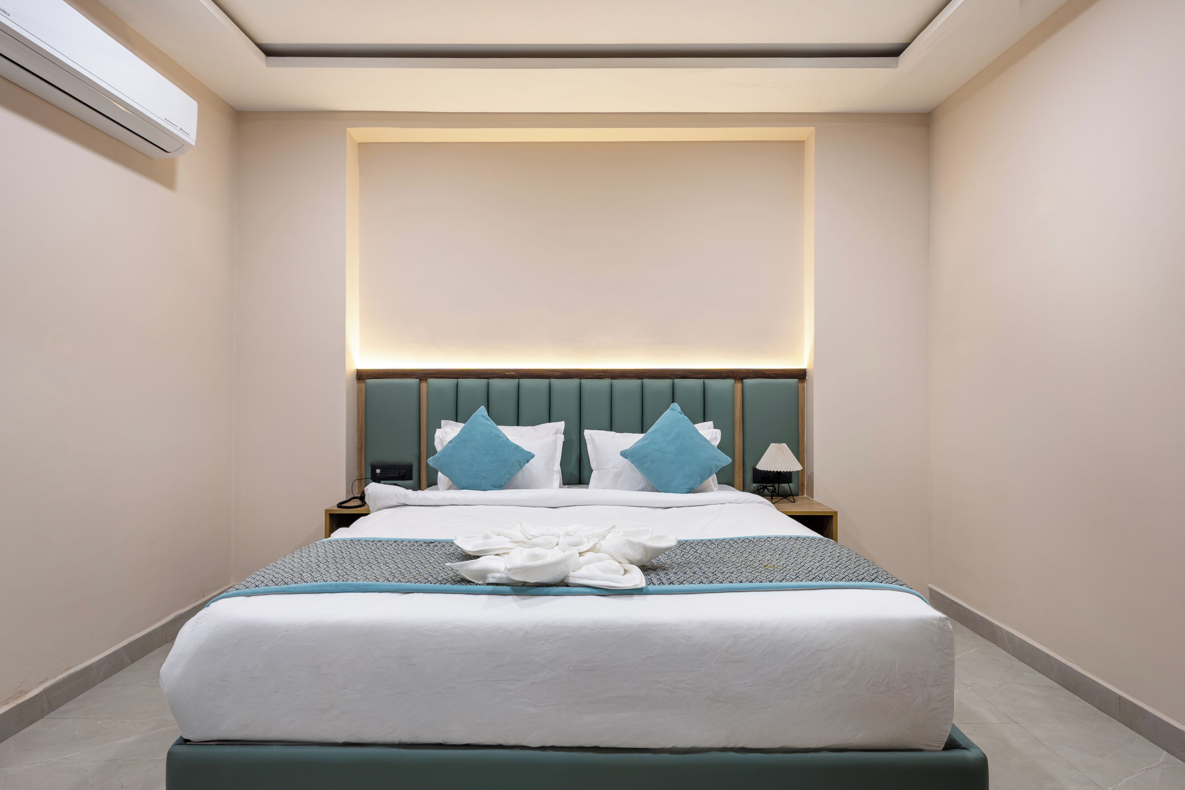 A hotel room with a large bed, a bedside table, a lamp, and a wall-mounted air conditioner.